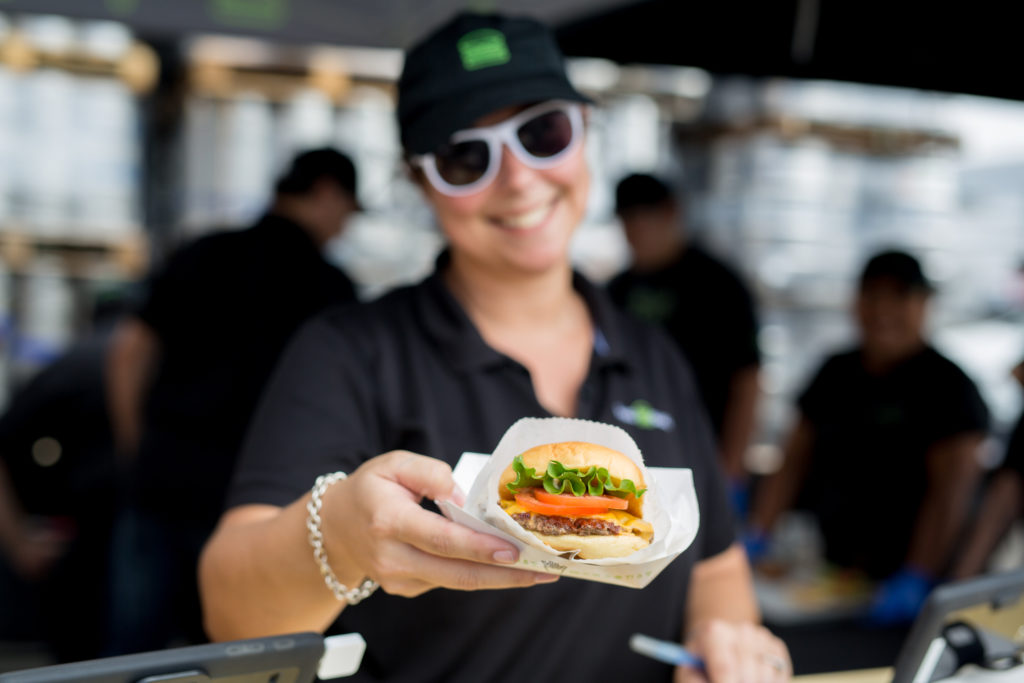 Employee with sunglasses holding out Shake Shack burger
