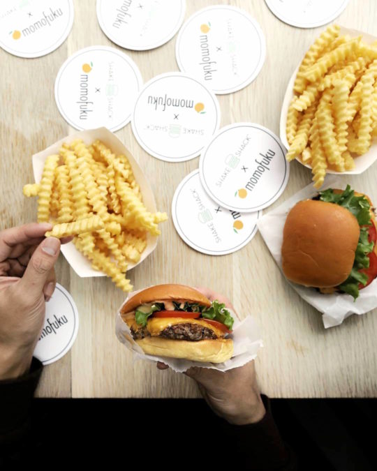 hand holding shake shack burger with other hand picking up a french fry