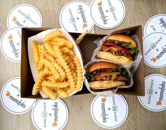 two burgers and fries with momofuku stickers on a table