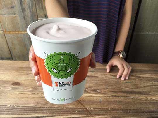 Great American Shake Sale Shake cup with shake being held out above wood table