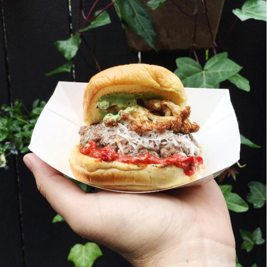 Shake Shack and Chef Lee Wolen's BOKA inspired burger being held out in hand with ingredients on display
