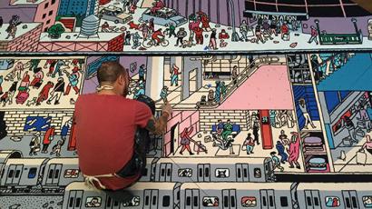 person crouched down painting an intricate mural on the ground.