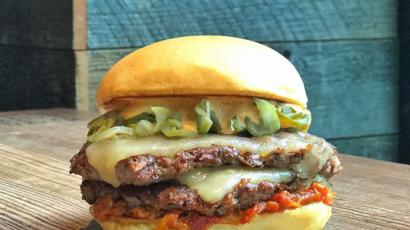 double burger with many toppings sitting on a wooden surface