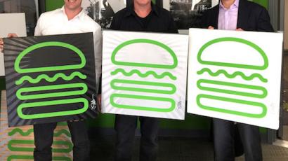 three people holding large, square signs with the shake shack logo on them.